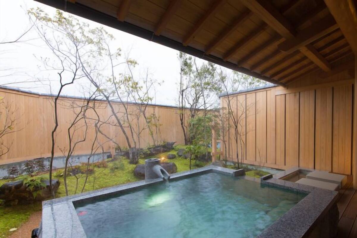 A hot tub in a wooden deck area with a view of trees and a wooden wall.