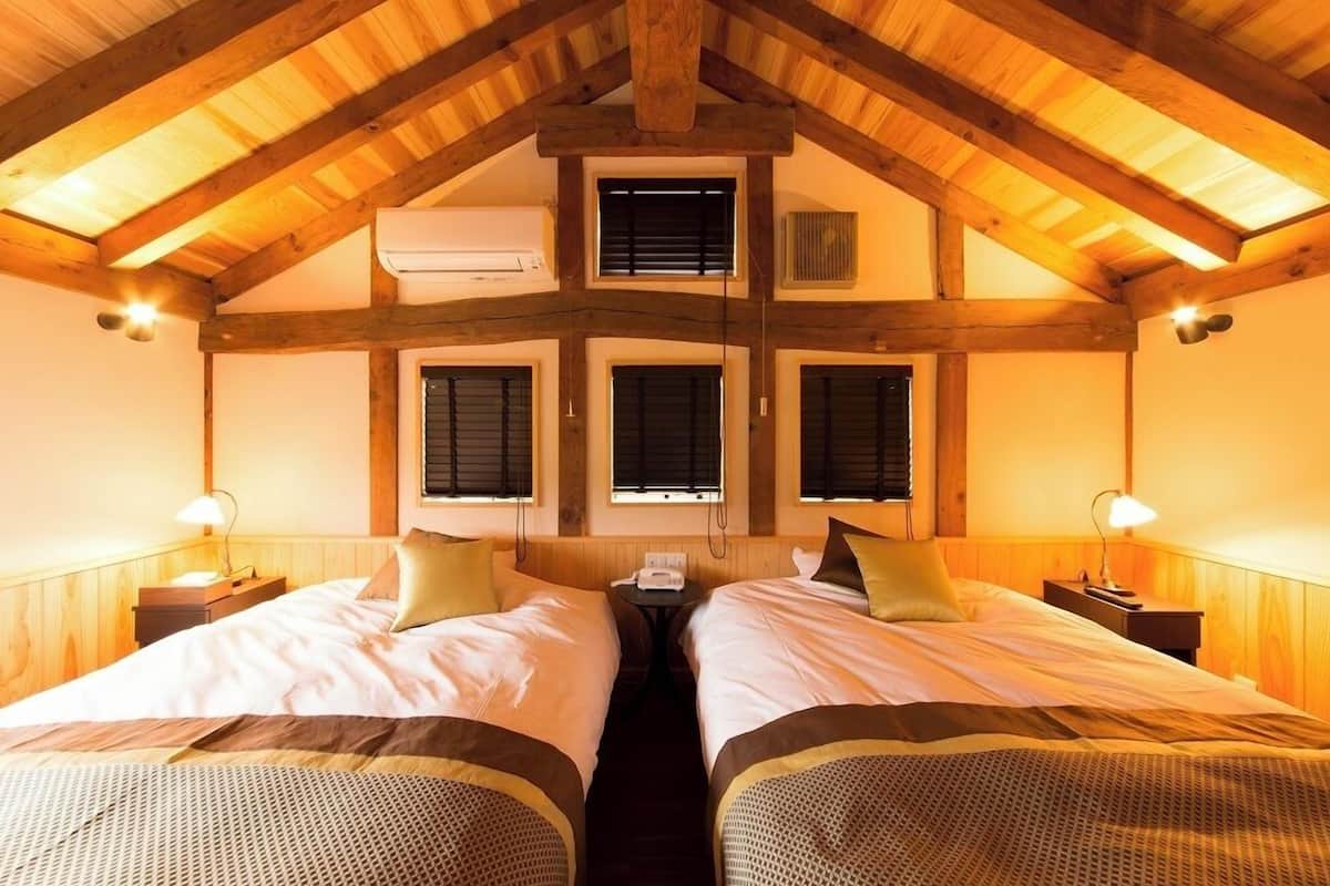 A room with two beds, wooden beams, and a central window.