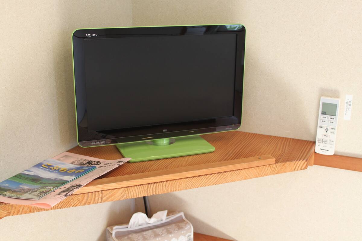 A flat-screen monitor on a wooden desk with a remote control and a tissue box.