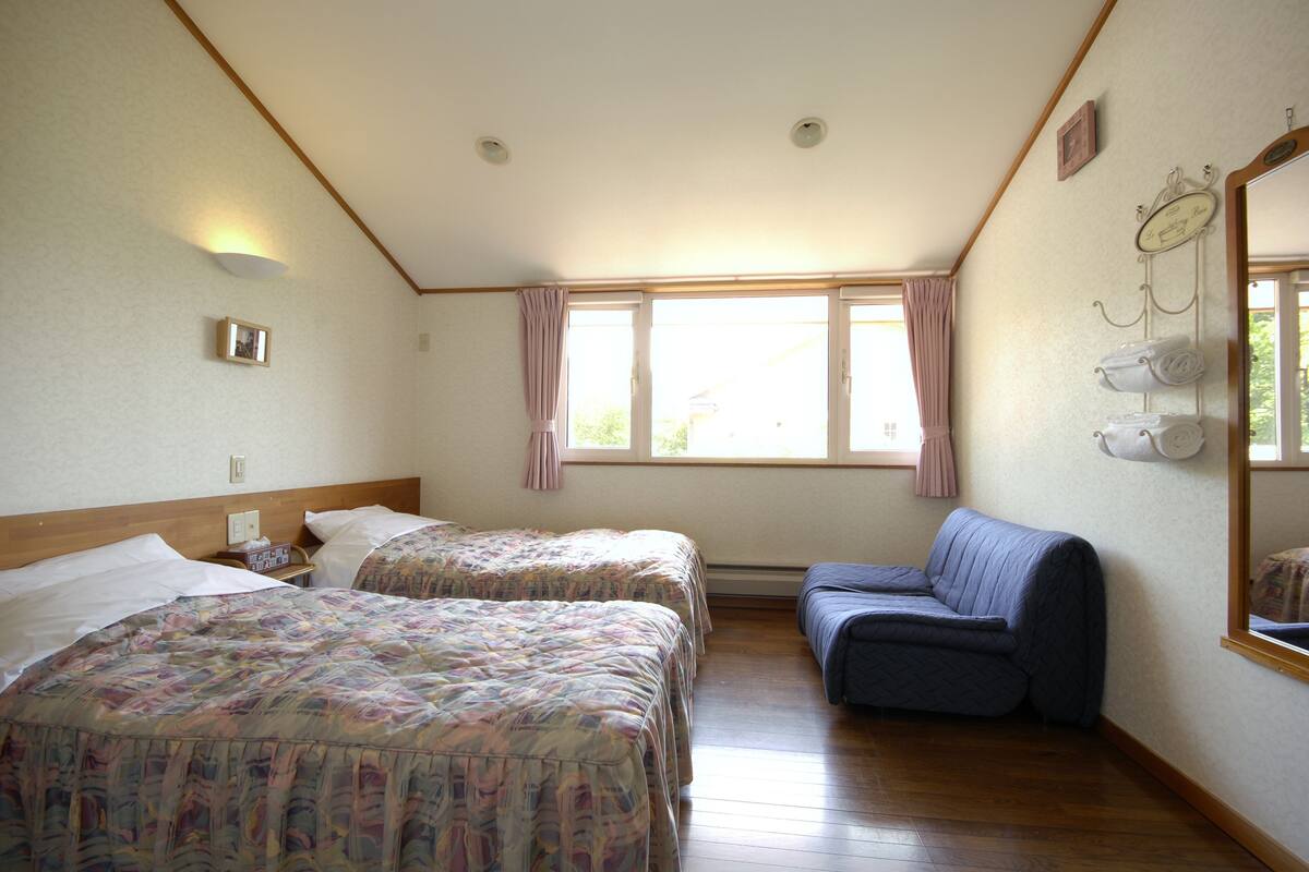 A hotel room with two beds, a sofa, a window with curtains, and a wall-mounted towel rack.