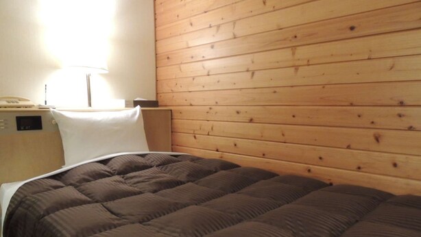 A single bed with a brown quilt, a wooden headboard, and a nightstand with a lamp. - Mitsukaido Dai Ichi Hotel (Joso)