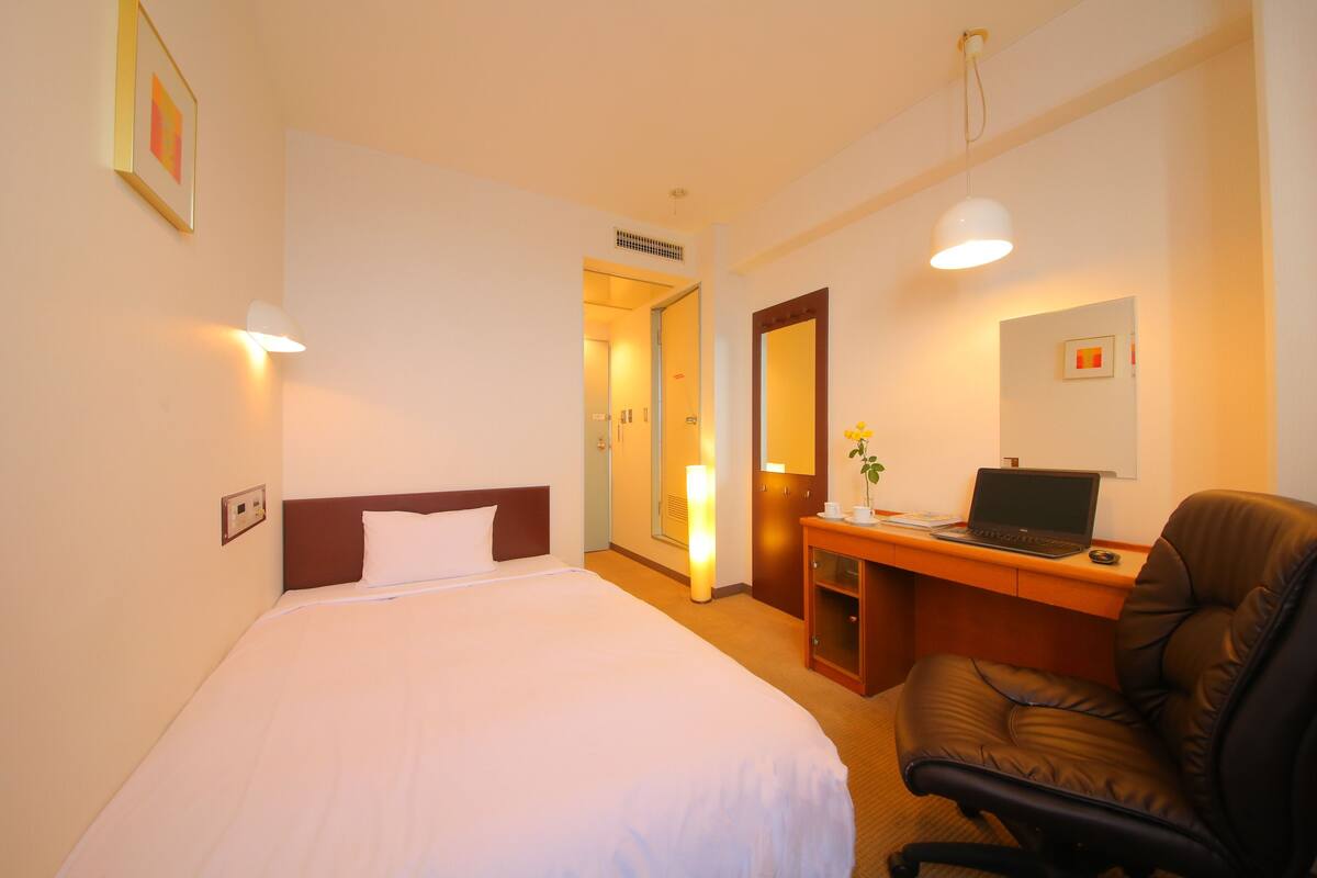 A hotel room with a bed, desk, chair, and a door leading to another room.
