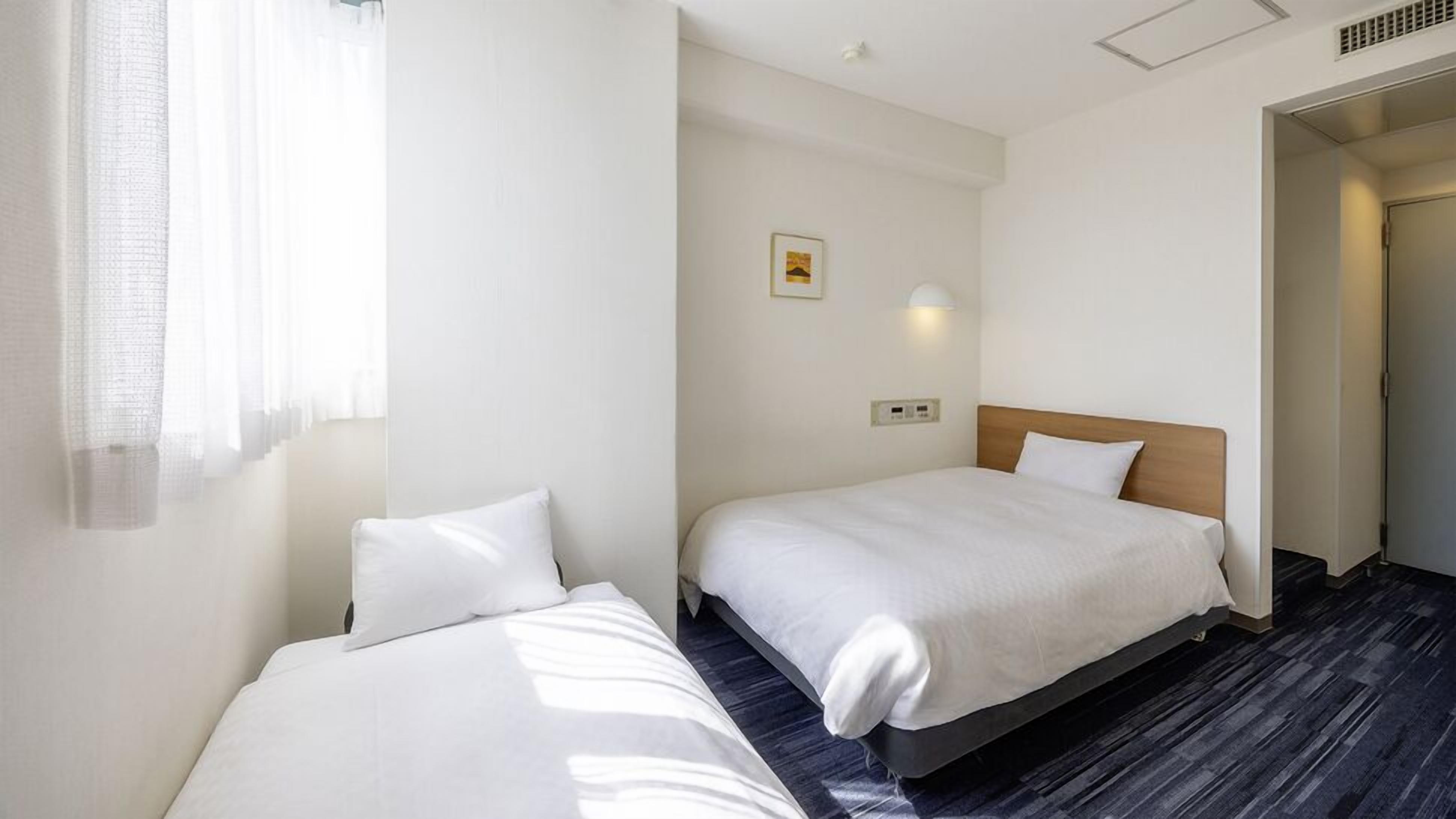 Habitación de hotel con dos camas individuales, una mesita de noche pequeña, una lámpara de pared e imagen decorativa en la pared.