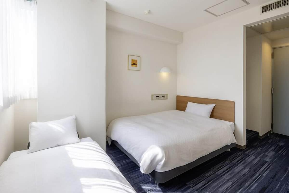 A hotel room with two single beds, a small bedside table, a wall-mounted light, and a picture on the wall.
