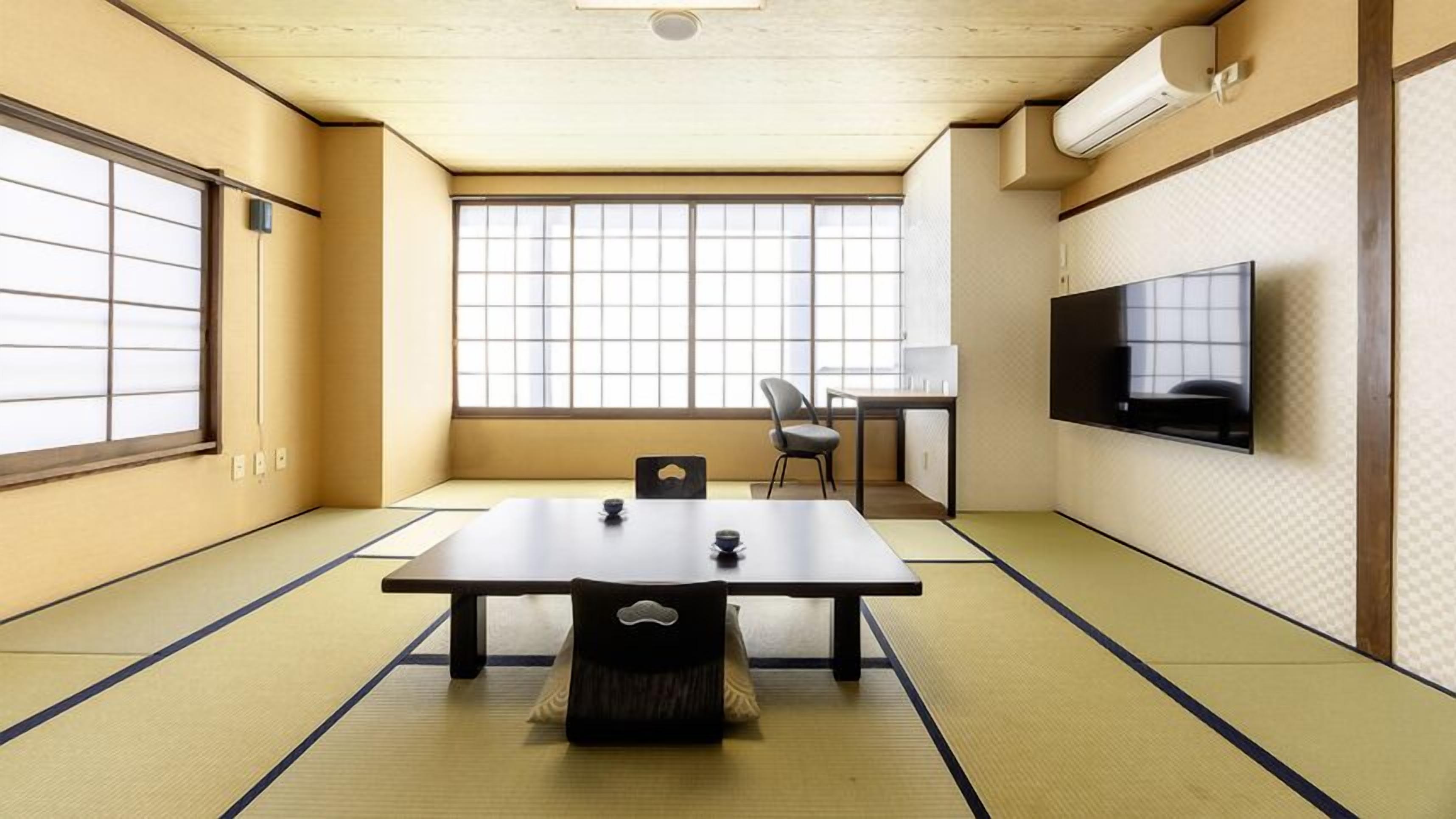 Una habitación con tatamis, una mesa baja, un televisor en la pared y una ventana con vistas.