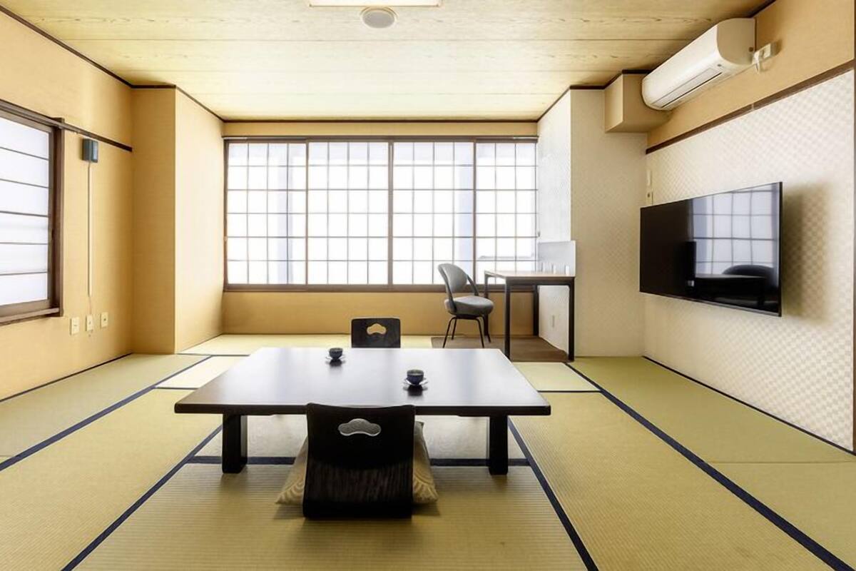 A tatami mat room with a low table, a TV on the wall, and a window with a view.