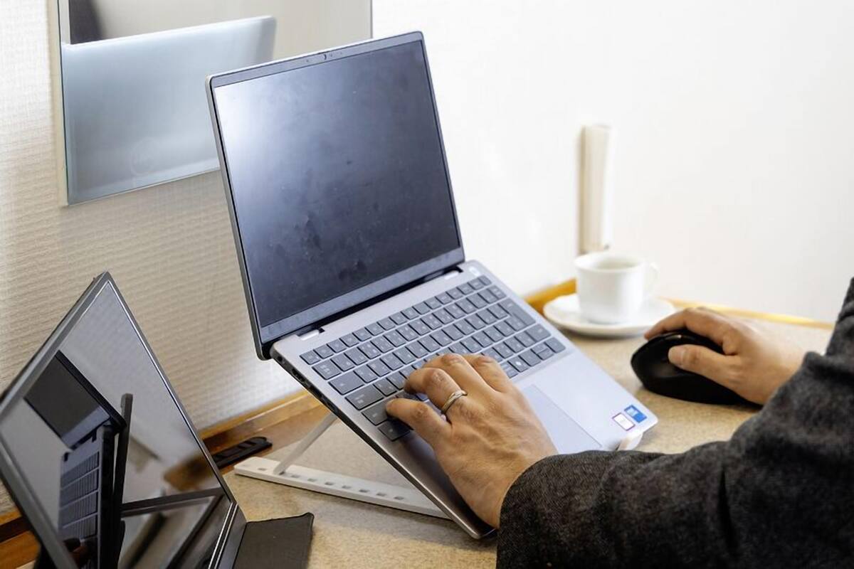 A person using a laptop on a desk with a cup and a mouse nearby.
