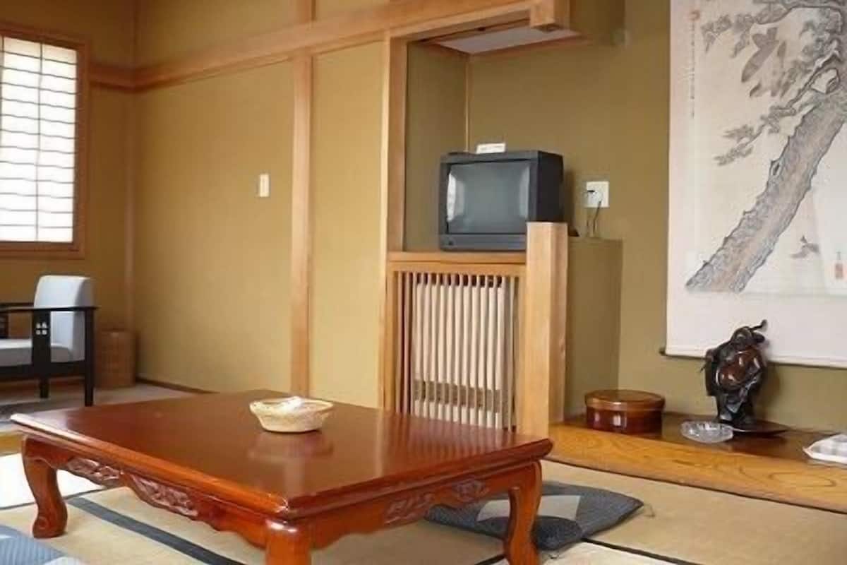 Una habitación japonesa tradicional con suelo de tatami, una mesa de madera baja, un televisor sobre un mueble y una pintura en la pared.