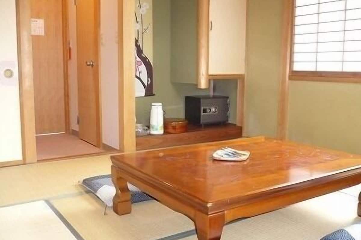 Una habitación japonesa tradicional con suelo de tatami, una mesa de madera, un mueble bajo y una puerta corrediza.