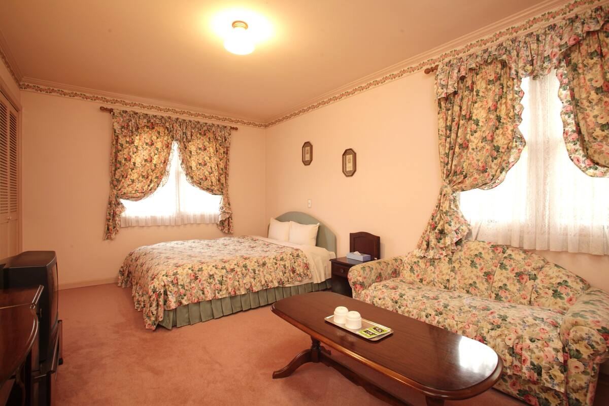 A room with two beds, a sofa, a wooden table, and a desk.