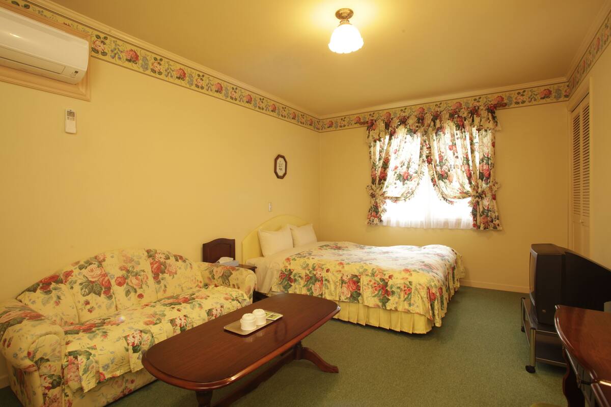 A room with floral-patterned furniture, a bed with floral curtains, a television, and a clock on the wall.