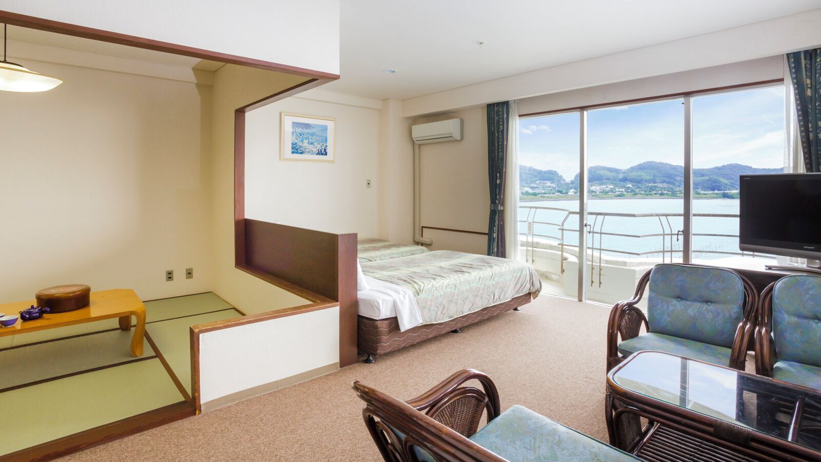 A hotel room with a bed, a television, a balcony with a view, and a dining area with chairs and a table.