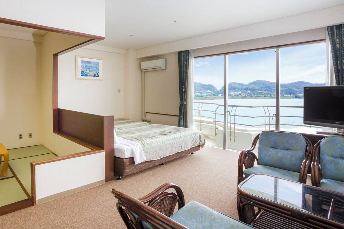 A hotel room with a bed, a television, a balcony with a view, and a dining area with chairs and a table.