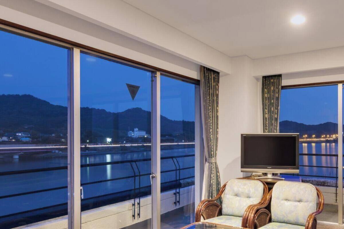 A room with large windows, a television, and a seating area with a view of a body of water and mountains.
