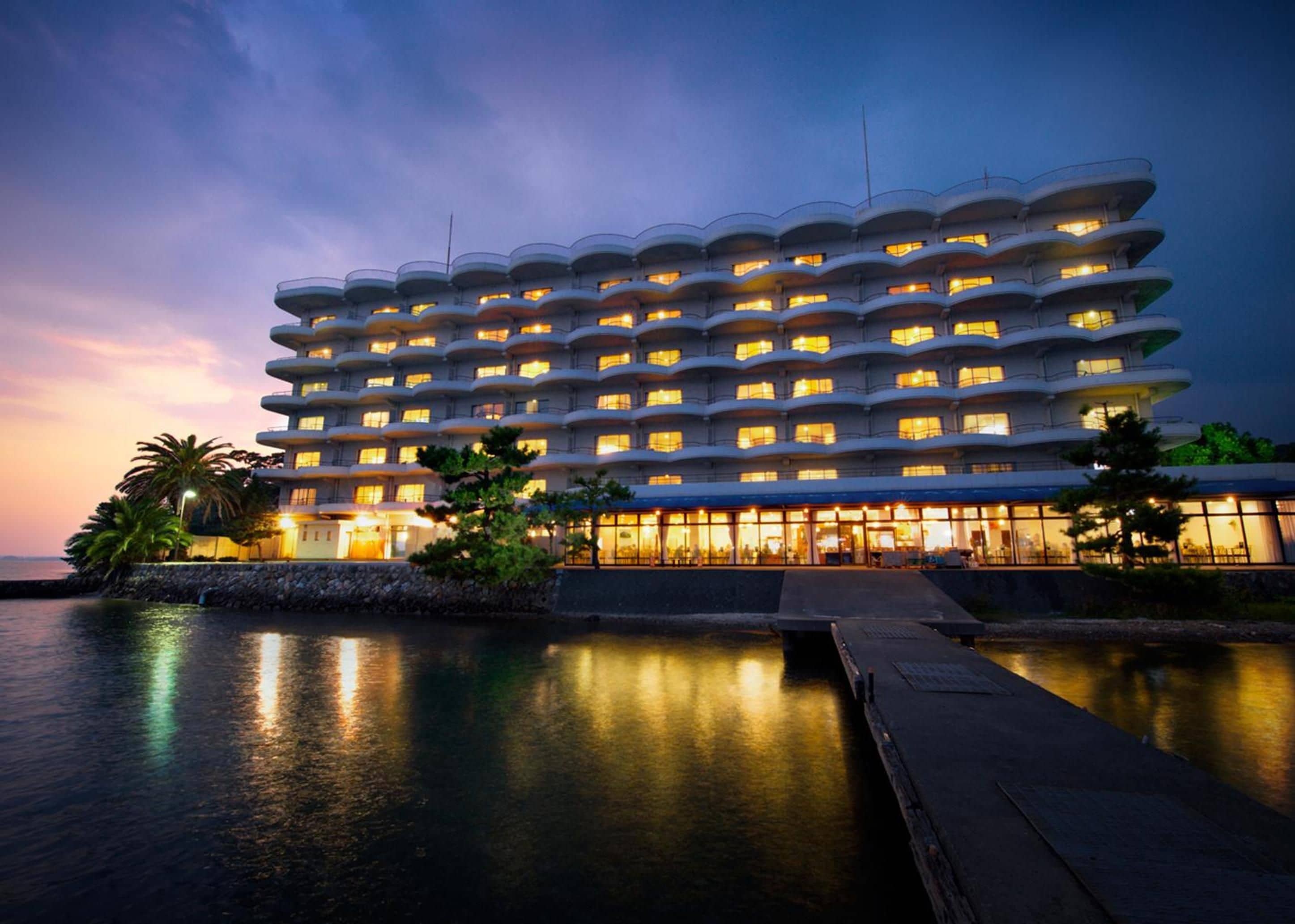 A multi-story hotel with balconies, a pool area, and a waterfront view.