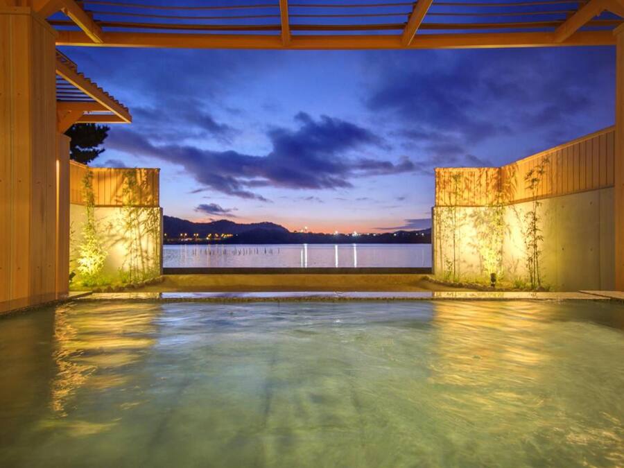 An outdoor swimming pool with a view of a body of water and mountains in the distance.