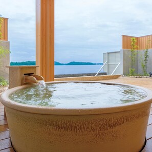 A large, round, beige outdoor hot tub with a wooden structure behind it, overlooking a body of water and distant land. - Hotel Green Plaza Hamanako (Hamamatsu)