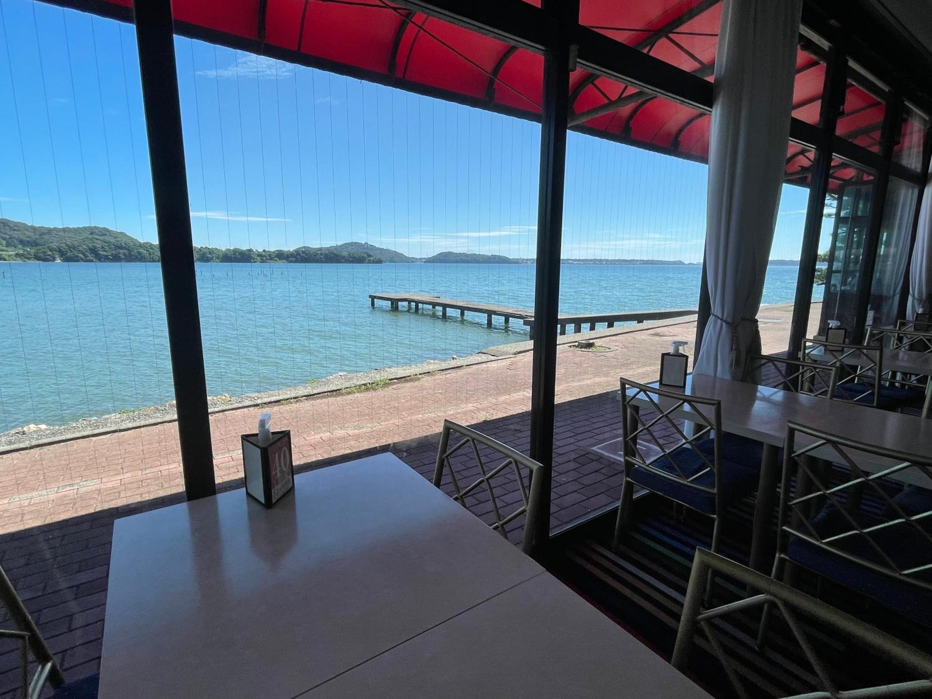 A terrace with a view of a lake and a pier, featuring tables and chairs.
