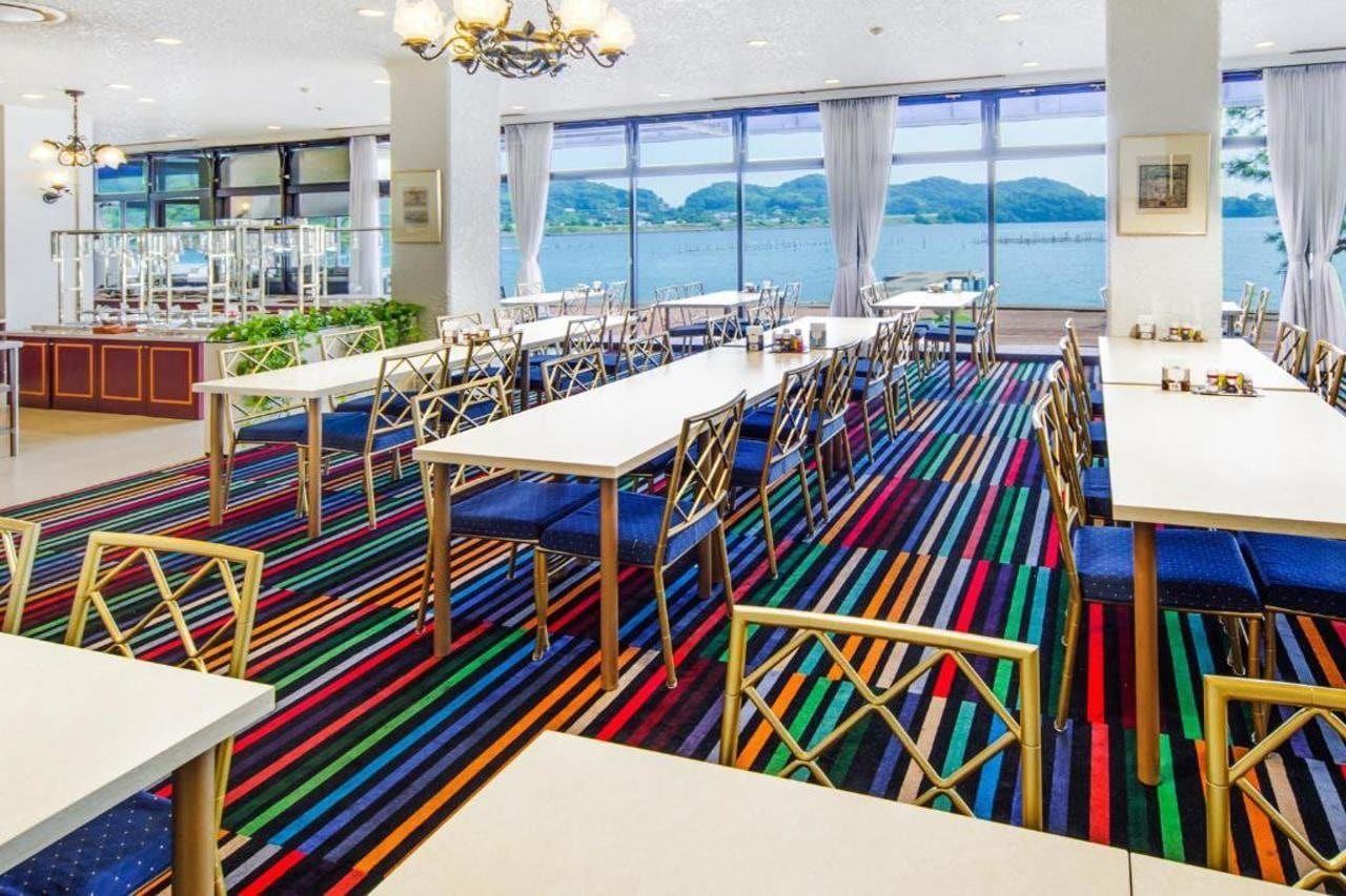 A dining area with tables and chairs, a patterned carpet, and a view of the water.