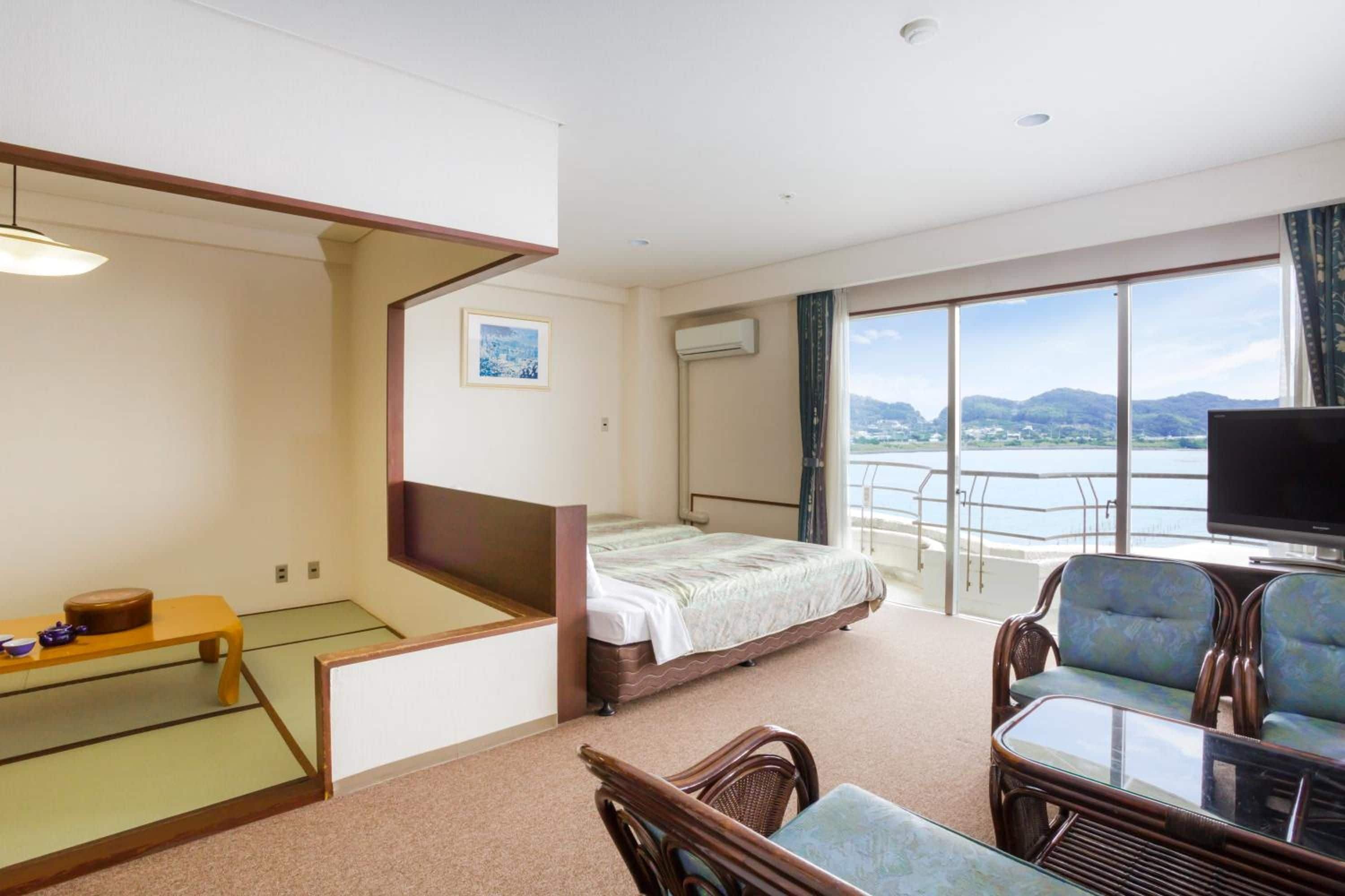 A hotel room with a bed, a television, a balcony with a view, and a seating area with chairs and a table.