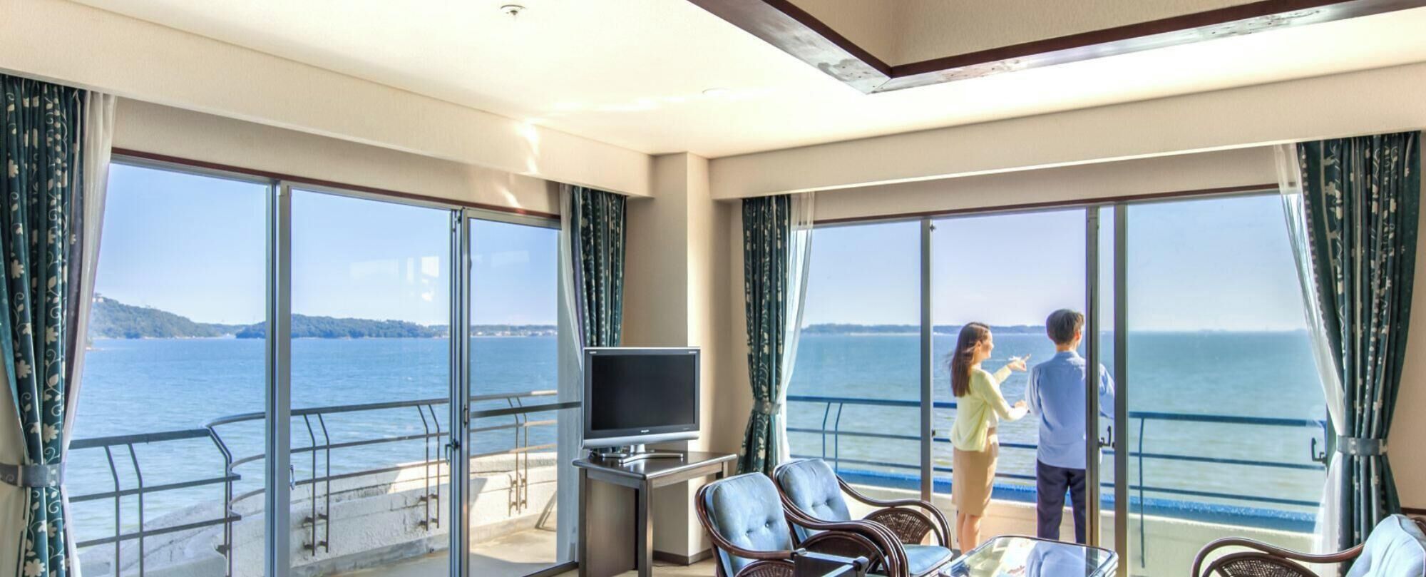 A balcony with a TV, seating, and a view of the sea.