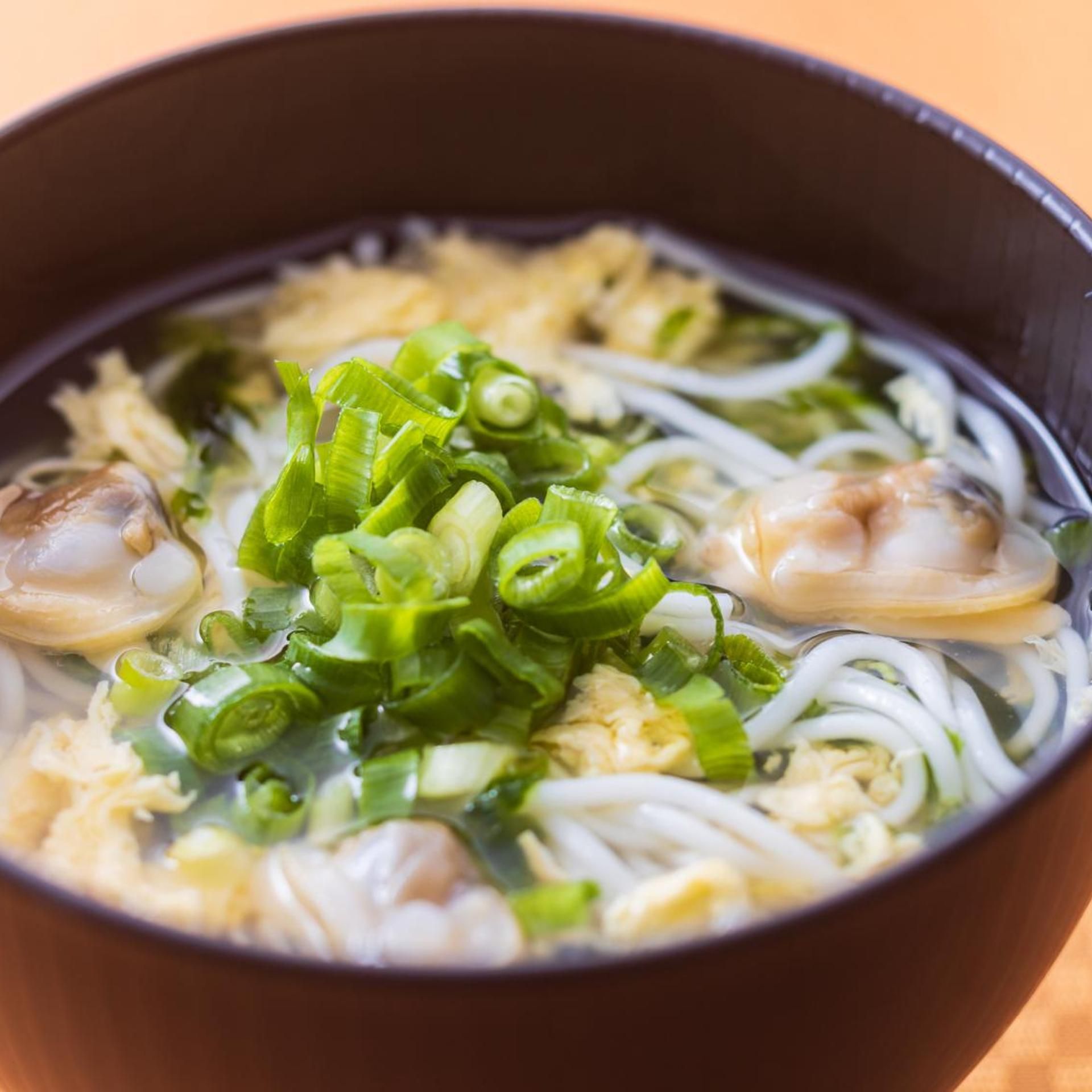 A bowl of soup with noodles, green onions, and shrimp.