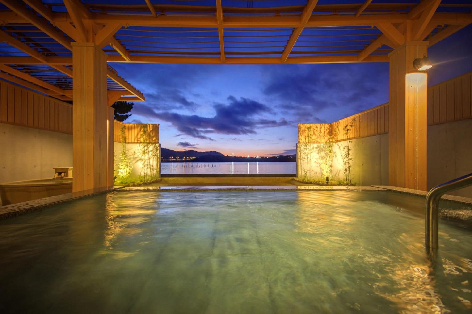 A hot tub area with a view of a body of water and mountains at dusk.