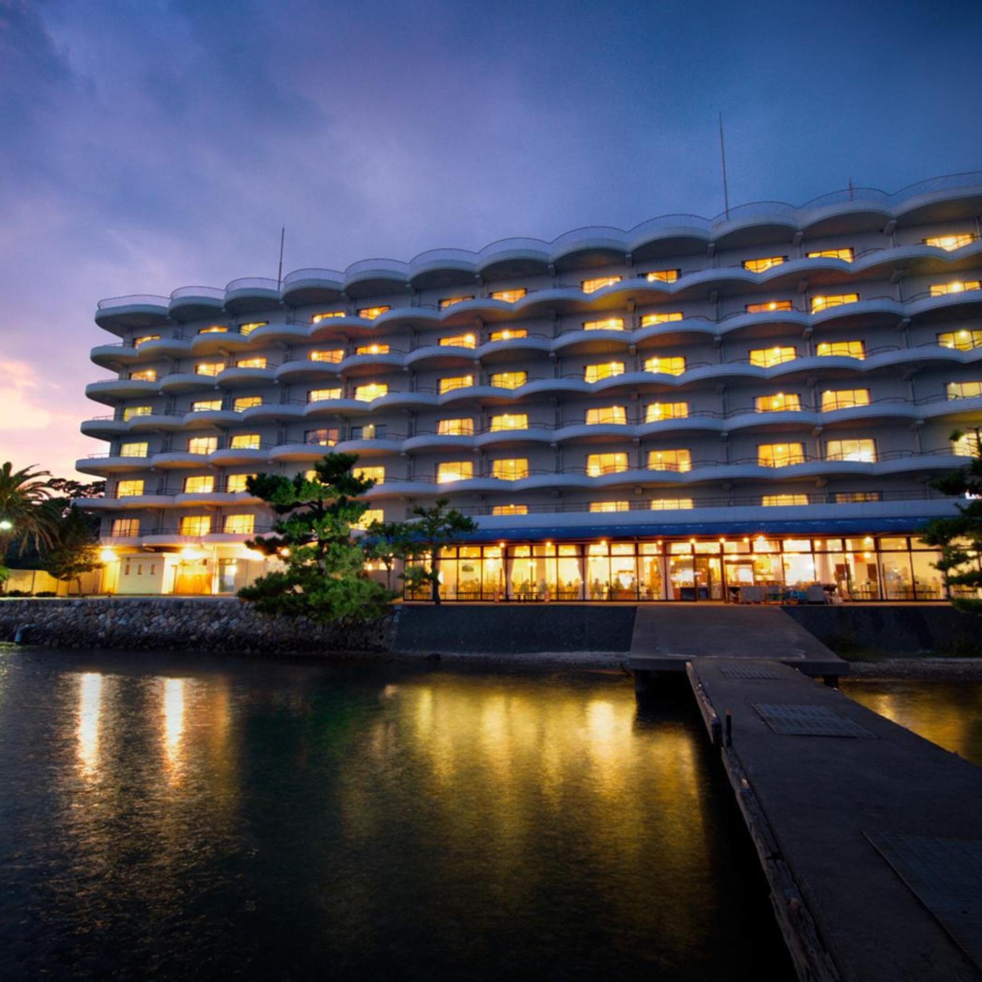 A multi-story hotel with balconies, a pool, and a waterfront view.