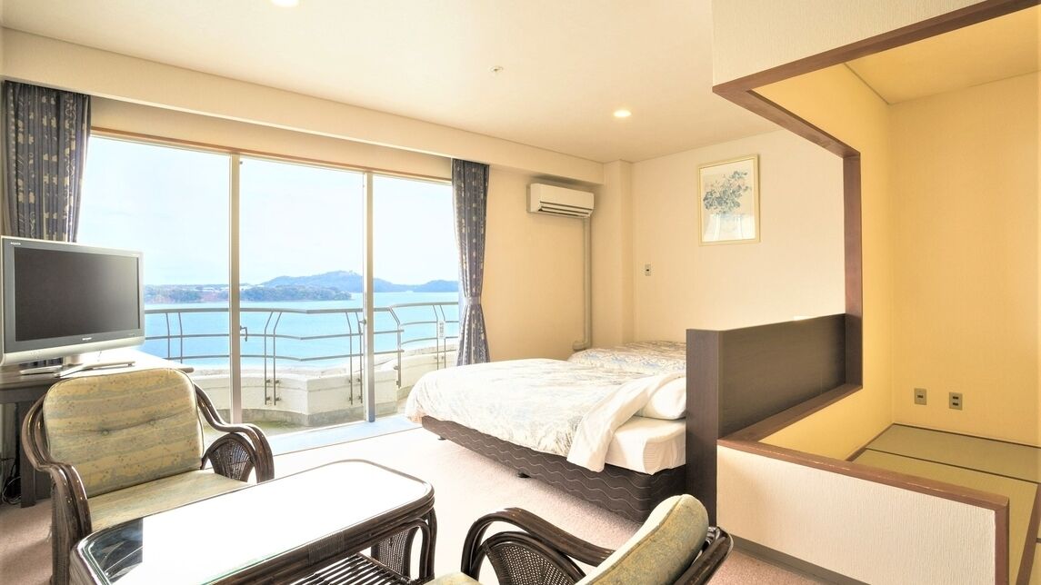 A hotel room with a bed, a TV, a balcony with a view, and a dining area with chairs.