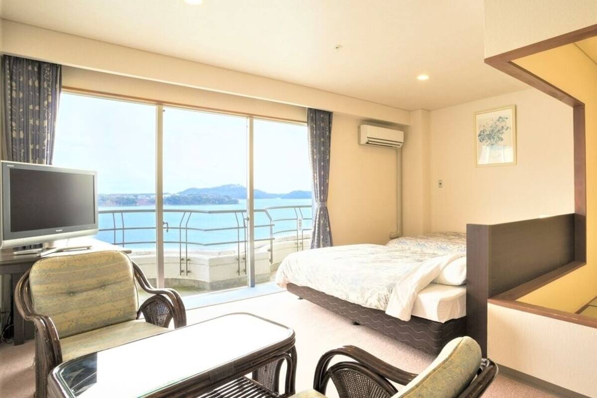 A hotel room with a bed, a TV, a balcony with a view, and a dining area with chairs.