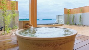A hot tub with a view of a lake, surrounded by wooden deck and plants. - Hotel Green Plaza Hamanako (Hamamatsu)