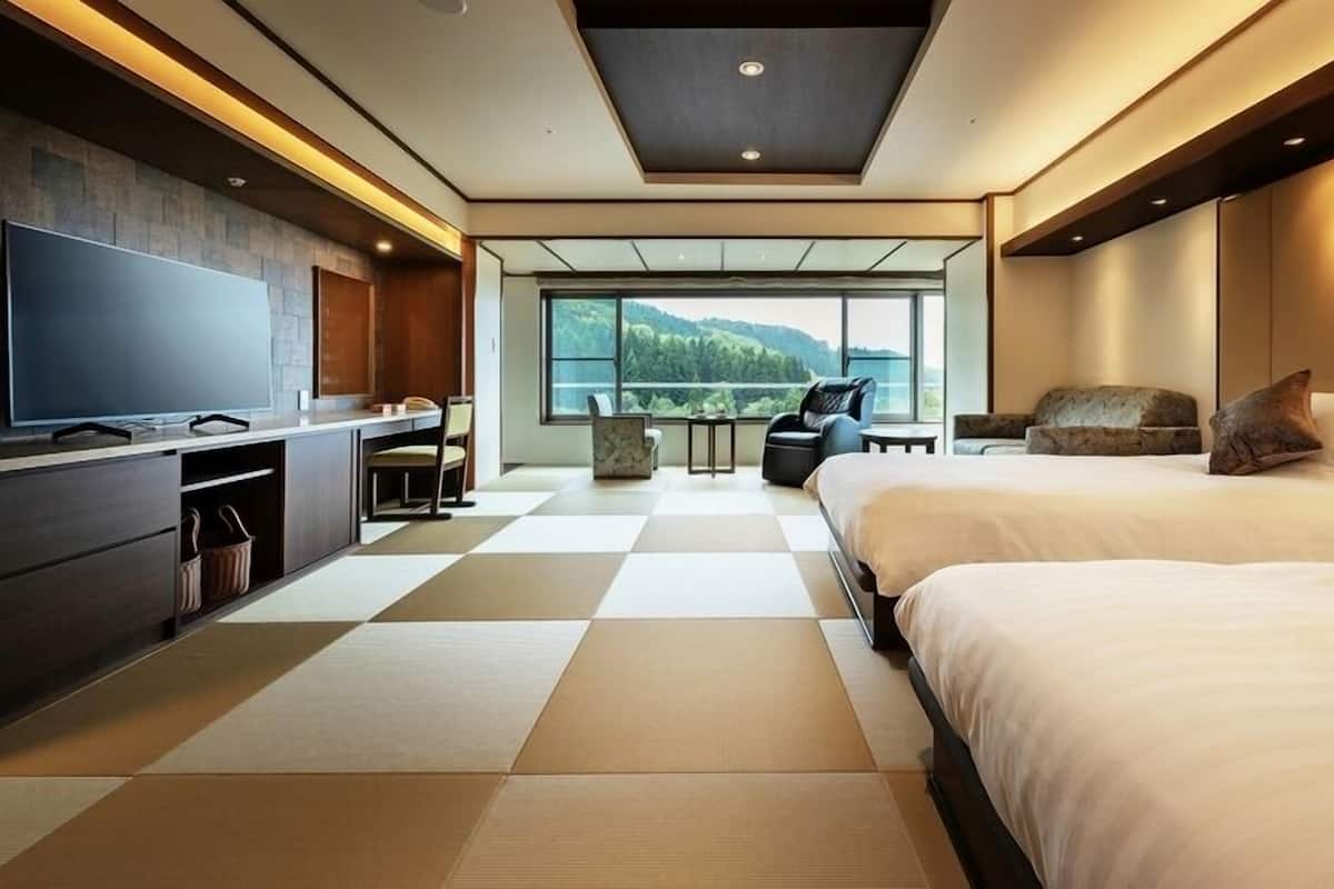 A modern hotel room with a large TV, a sofa, a bed, and a view of the outdoors.