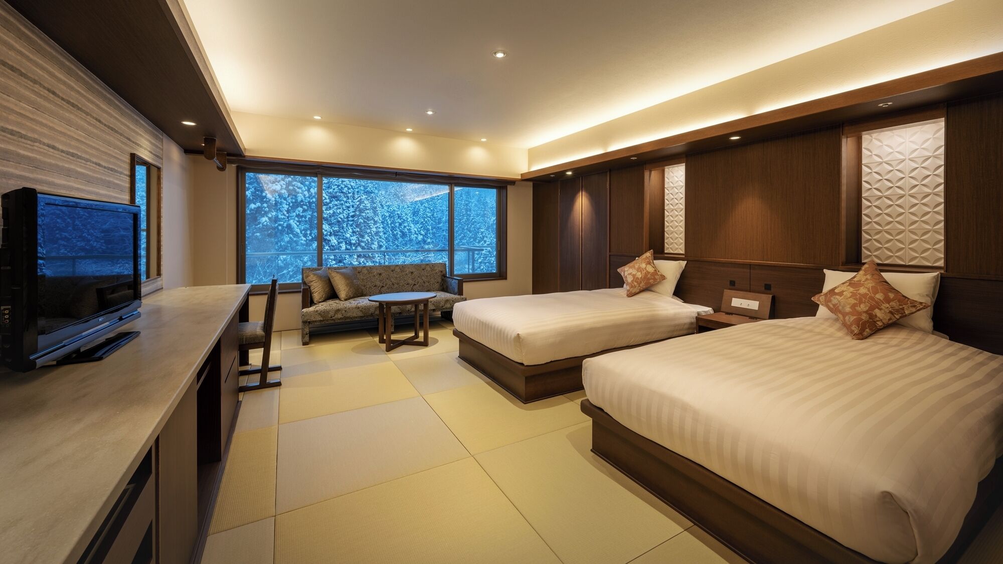 A modern hotel room with a large bed, a sofa, a TV, and a view of snow-covered trees.