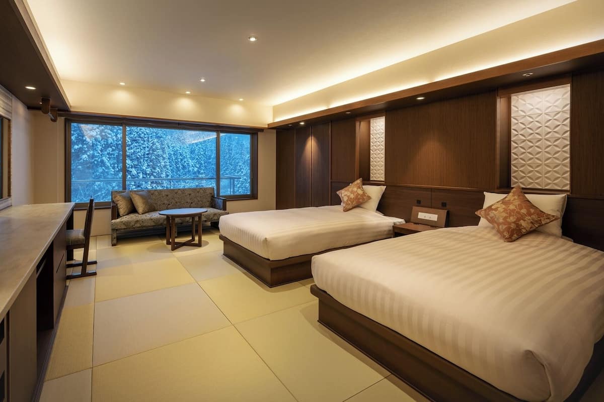 A modern hotel room with a large bed, a sofa, a TV, and a view of snow-covered trees.