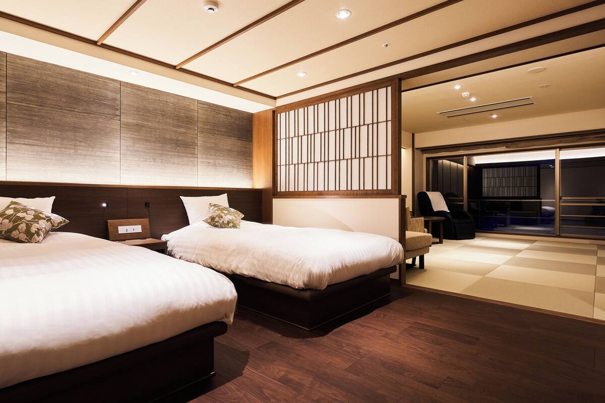 A hotel room with two beds, a large window, and a sliding door leading to a balcony.
