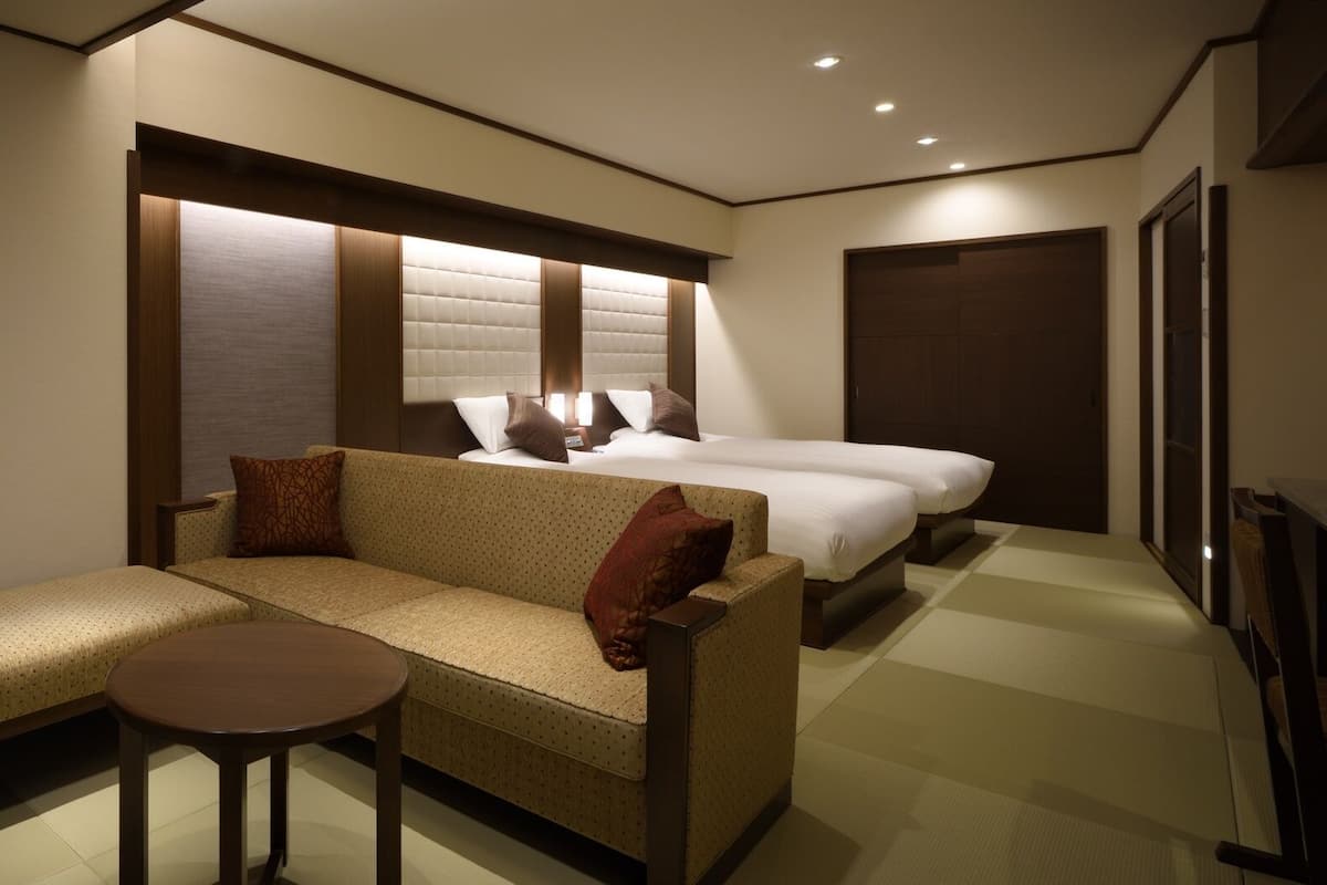 A hotel room with a sofa, a small table, a bed, and a wardrobe.