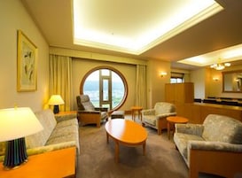 Une chambre d’hôtel équipée d’un canapé, de fauteuils, d’une table basse, d’un bureau et offrant une vue sur l’extérieur grâce à une grande fenêtre.