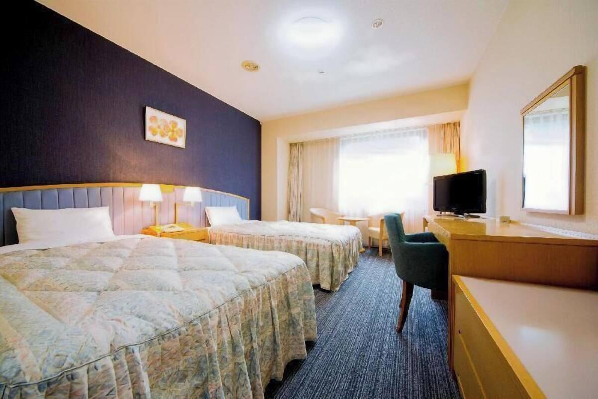 A hotel room with two beds, a desk, a chair, a television, and a window with curtains.
