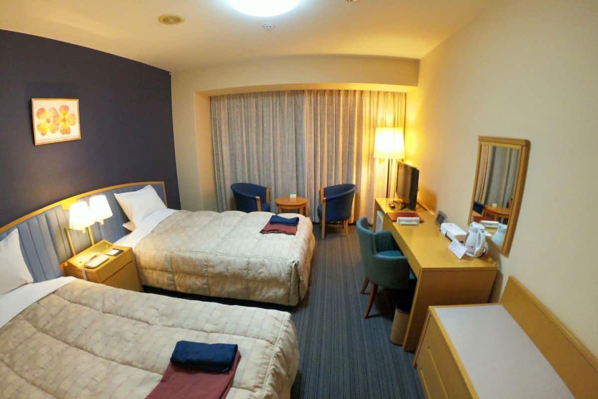 A hotel room with two beds, a desk, a chair, a TV, and a mirror.