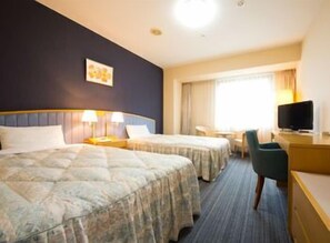 Habitación de hotel con dos camas, un escritorio con silla, televisión y ventana con cortinas.