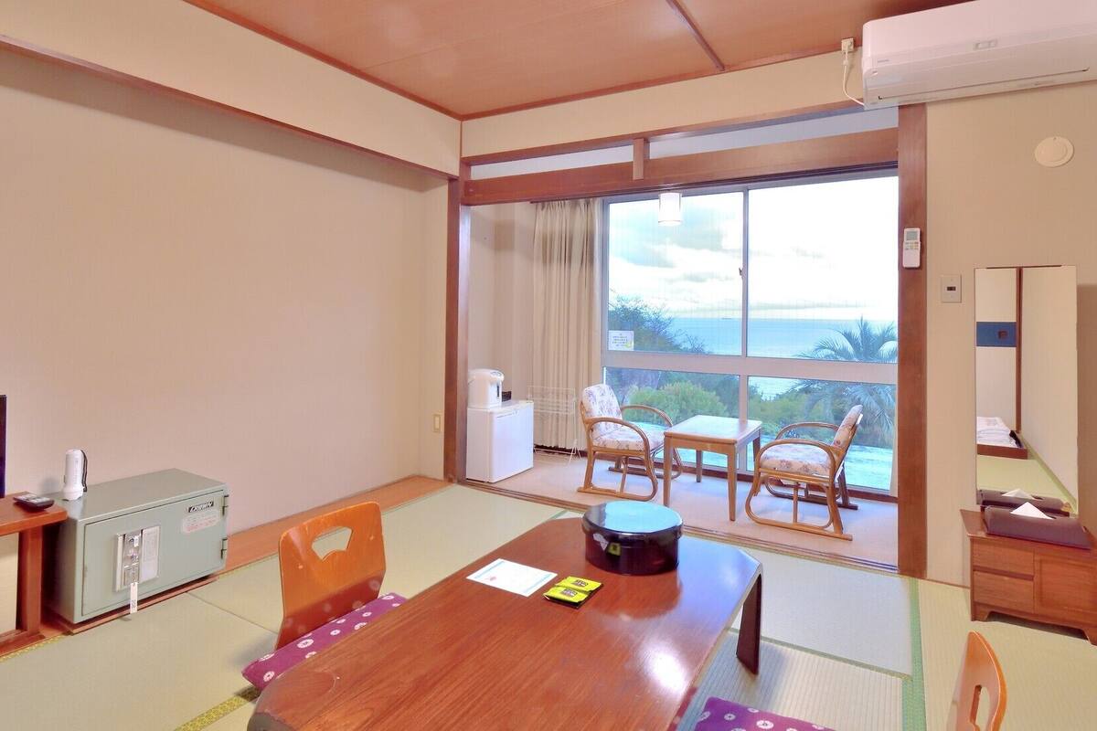 Une chambre d’hôtel avec une table à manger en bois, des chaises, une télévision, un minibar et une vue sur l’océan.