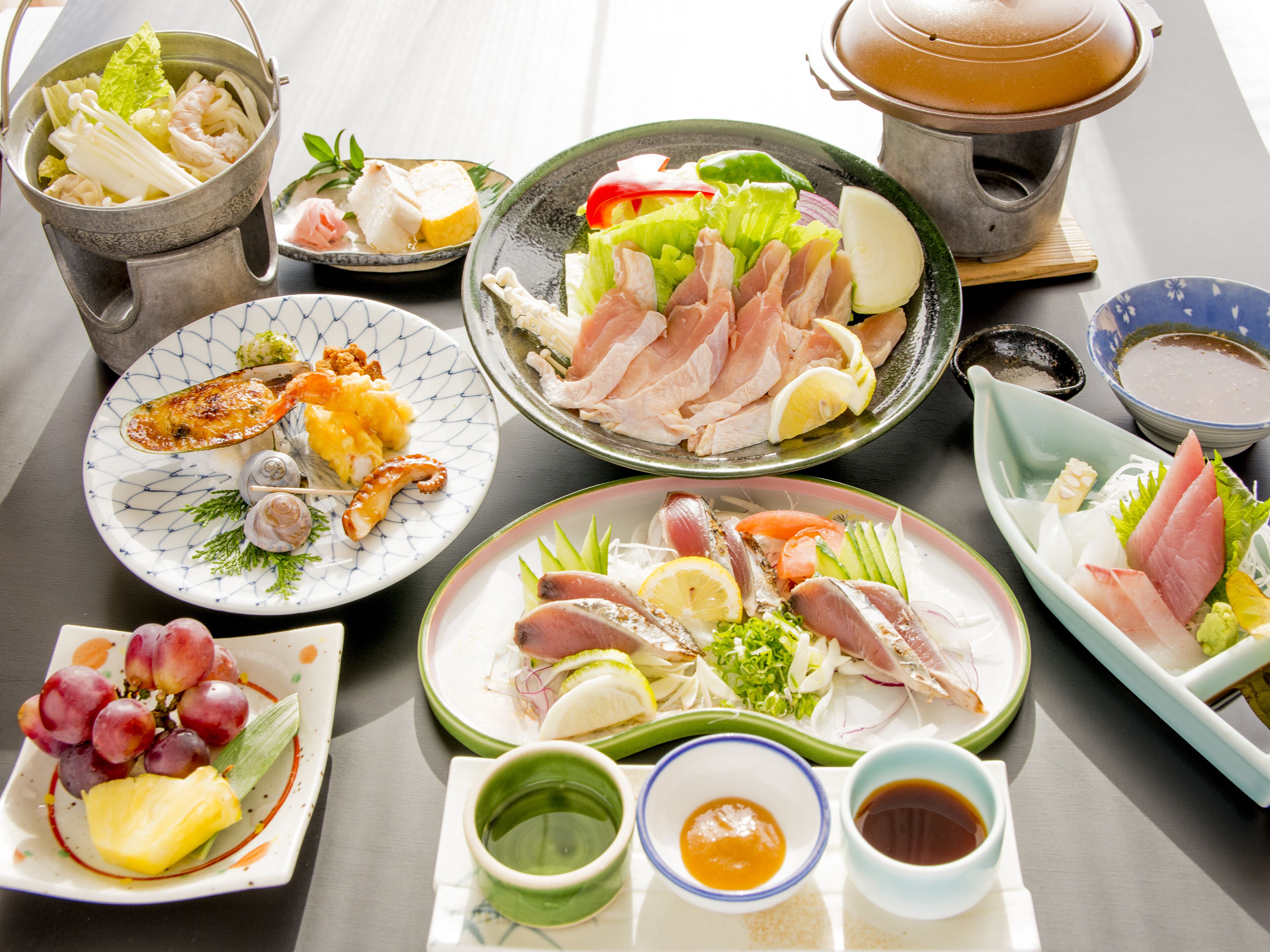 A variety of dishes including sashimi, seafood, and vegetables, arranged on a table.
