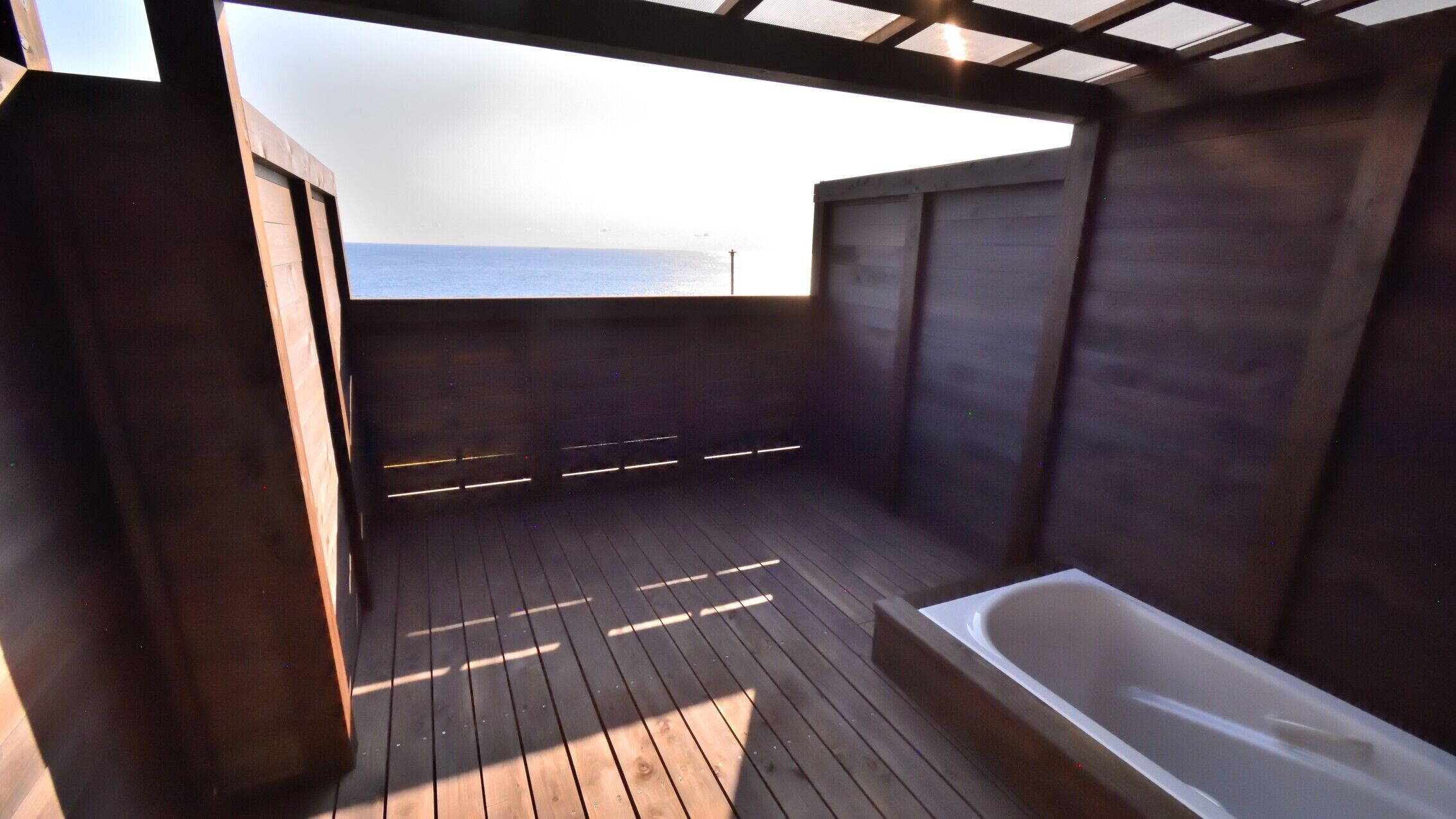 Una terraza de madera con una bañera y vista al océano.