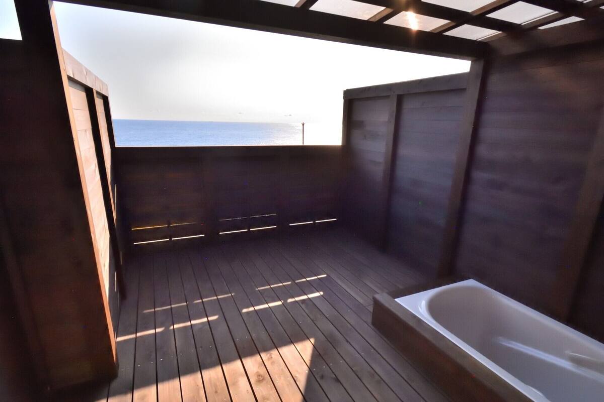 Une terrasse en bois avec une baignoire et une vue sur l’océan.