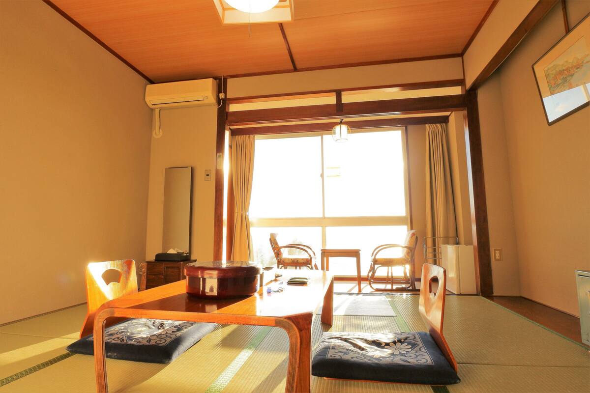 Une pièce de style japonais traditionnel, avec des tatamis, une table en bois et une porte coulissante donnant sur un balcon.