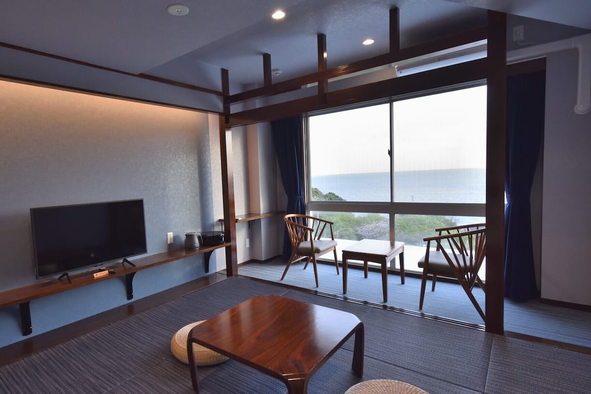 Een moderne hotelkamer met een groot raam, een flatscreen televisie, een houten tafel en een zithoek met stoelen.