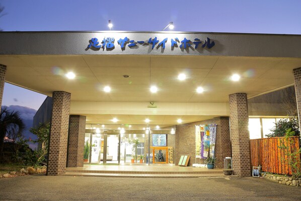 Entrada de un edificio con un letrero en japonés, pilares de ladrillo y plantas en macetas.