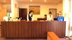 A reception desk with a digital clock displaying the time, a framed landscape painting on the wall, and a wooden counter. - Hotel Innoshima (Onomichi)