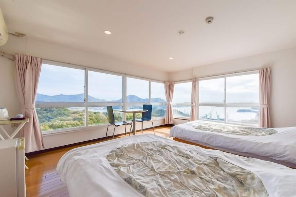 A hotel room with two beds, a desk, a chair, and large windows offering a view of the landscape.