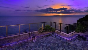 A balcony with a stone pathway, a stone lantern, and a view of the sea at sunset. - Atagawa Onsen Suiko (Higashiizu)